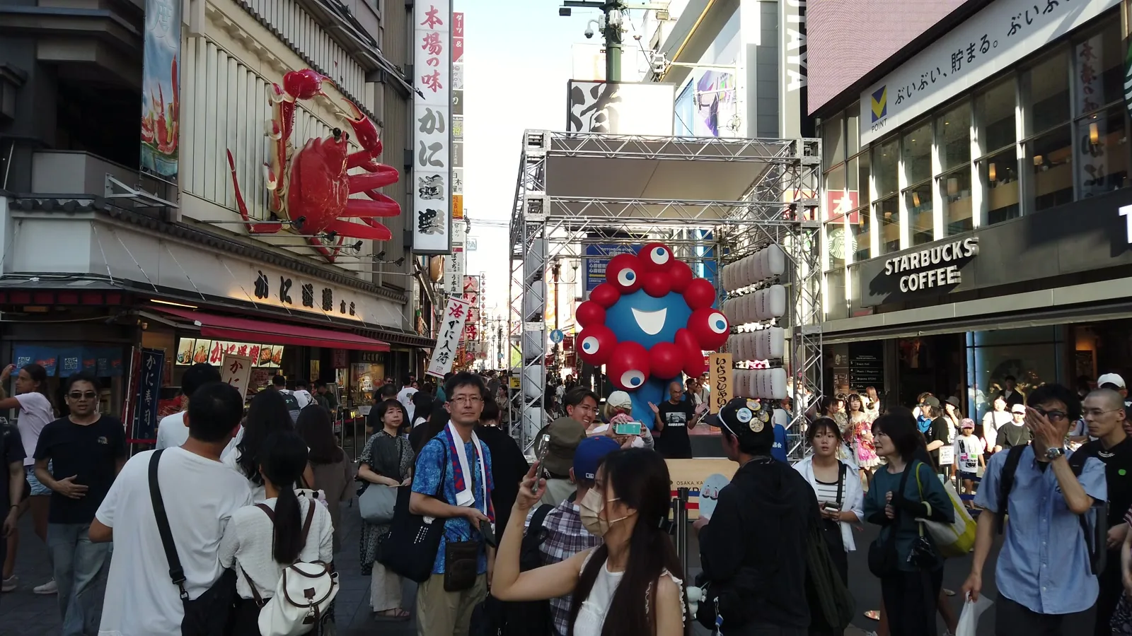 道頓堀の通りに立つミャクミャクの像と、その前で写真を撮る大勢の人たち