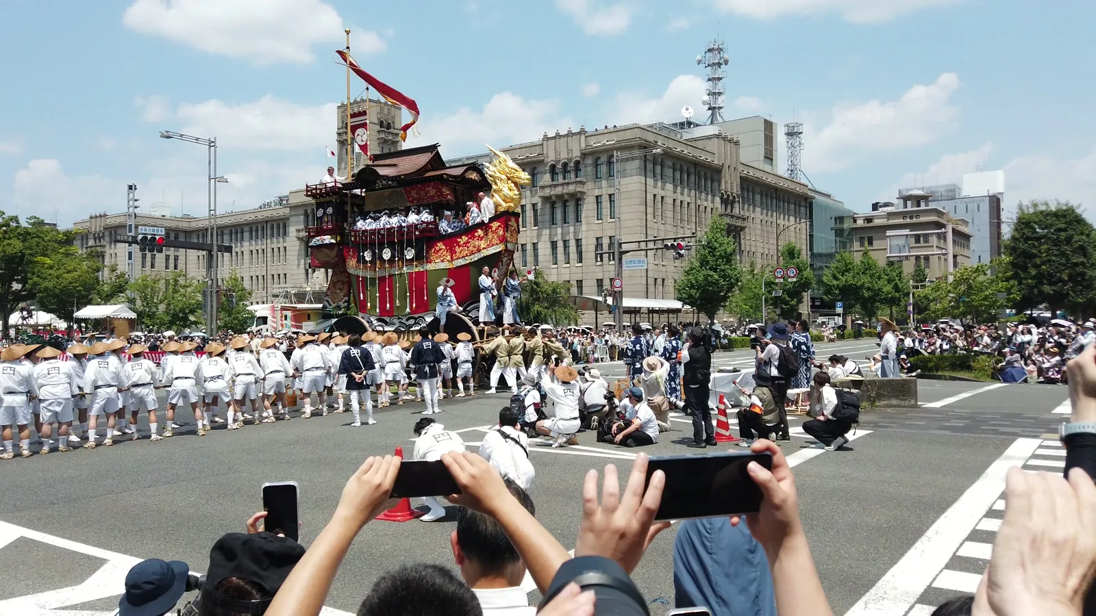 京都市役所前の交差点を進む祇園祭後祭の大船鉾と、菅笠をかぶった曳き手の長い列