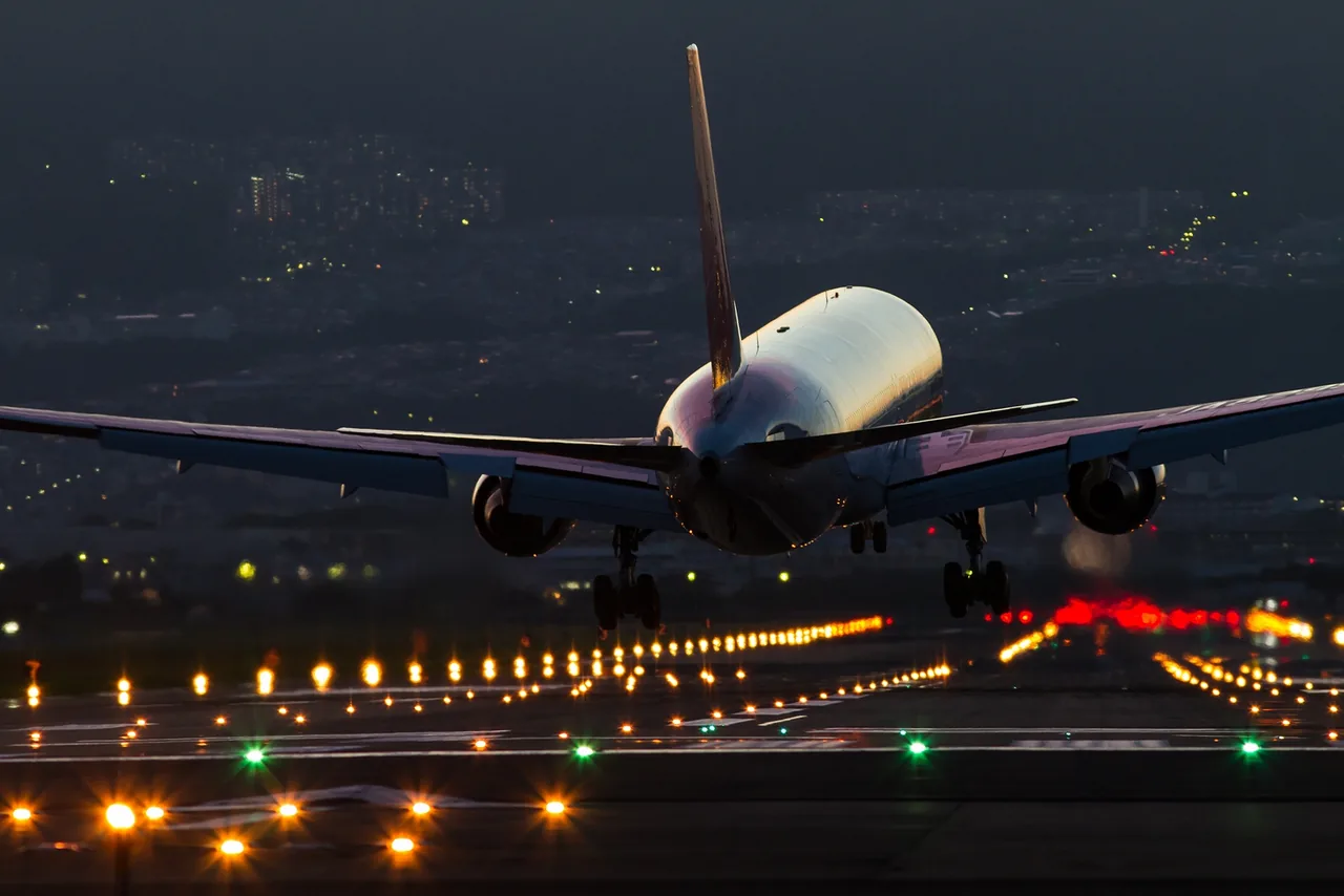夜の伊丹空港に着陸する日本航空の旅客機。着陸灯の光と滑走路の灯りが並ぶ