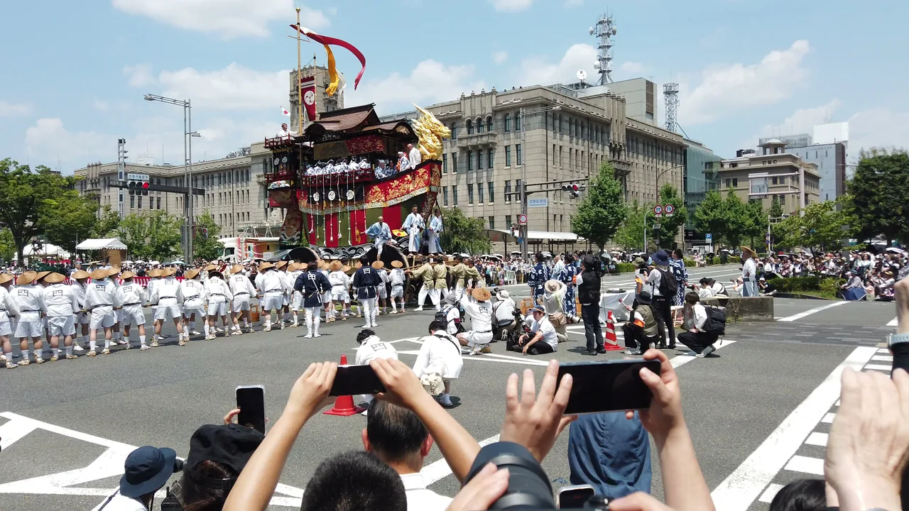 交差点で停止した山鉾と、いっせいにスマートフォンを掲げる見物客
