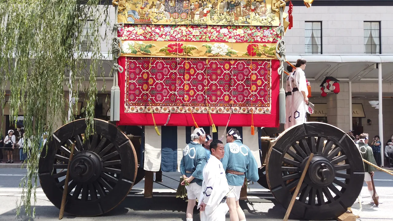 山鉾の巨大な木製車輪と、金糸で織られた懸装品を間近から見上げた様子