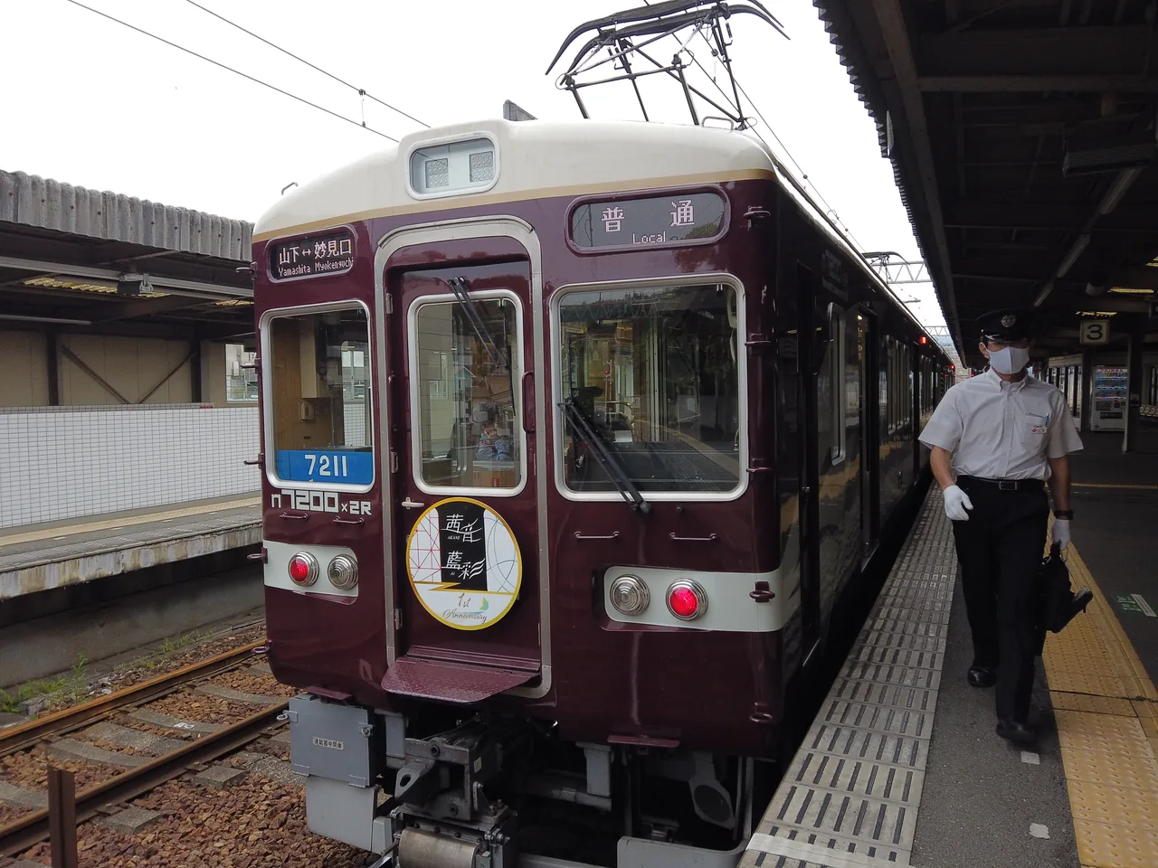 駅に停まるマルーン色の能勢電鉄の車両。「山下↔妙見口」「普通」の表示と、7211・n7200×2Rの車号が見える