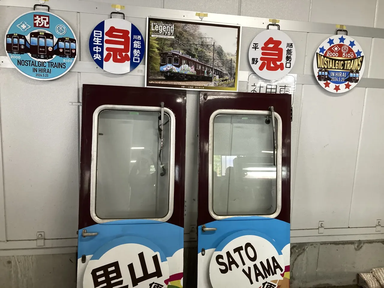 車両の扉に取り付けられた「里山」「黒山」などのヘッドマークが並ぶ展示