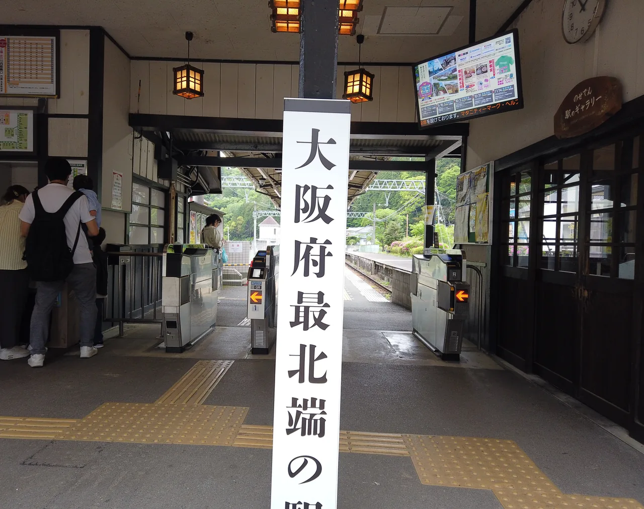 「大阪府最北端の駅」と書かれた白い柱が立つ妙見口駅の改札口。灯篭を模した照明と自動改札機が並ぶ