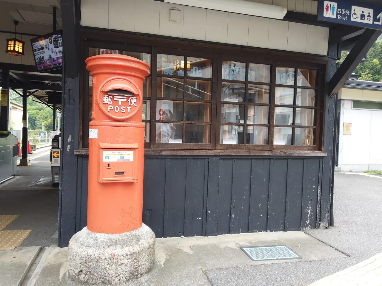 木造駅舎の前に立つ赤い丸型郵便ポスト