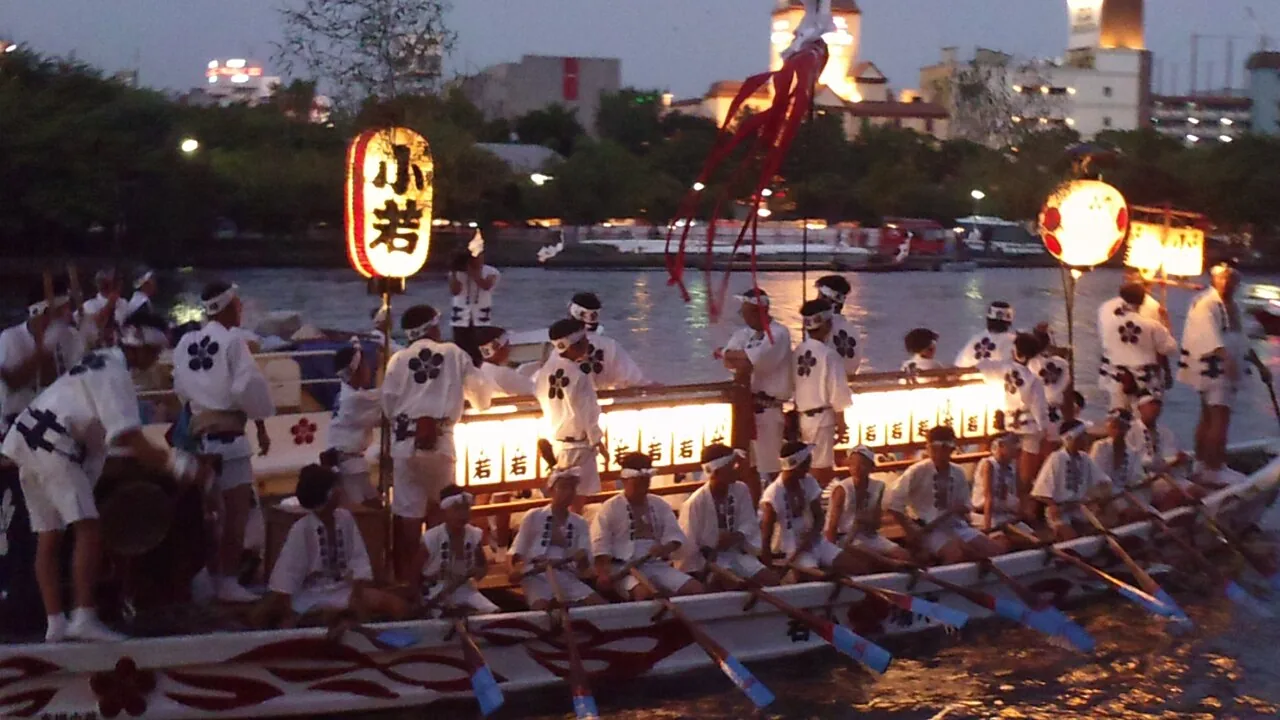 夕暮れの大川を、提灯を灯した船が列をなして進む天神祭の船渡御