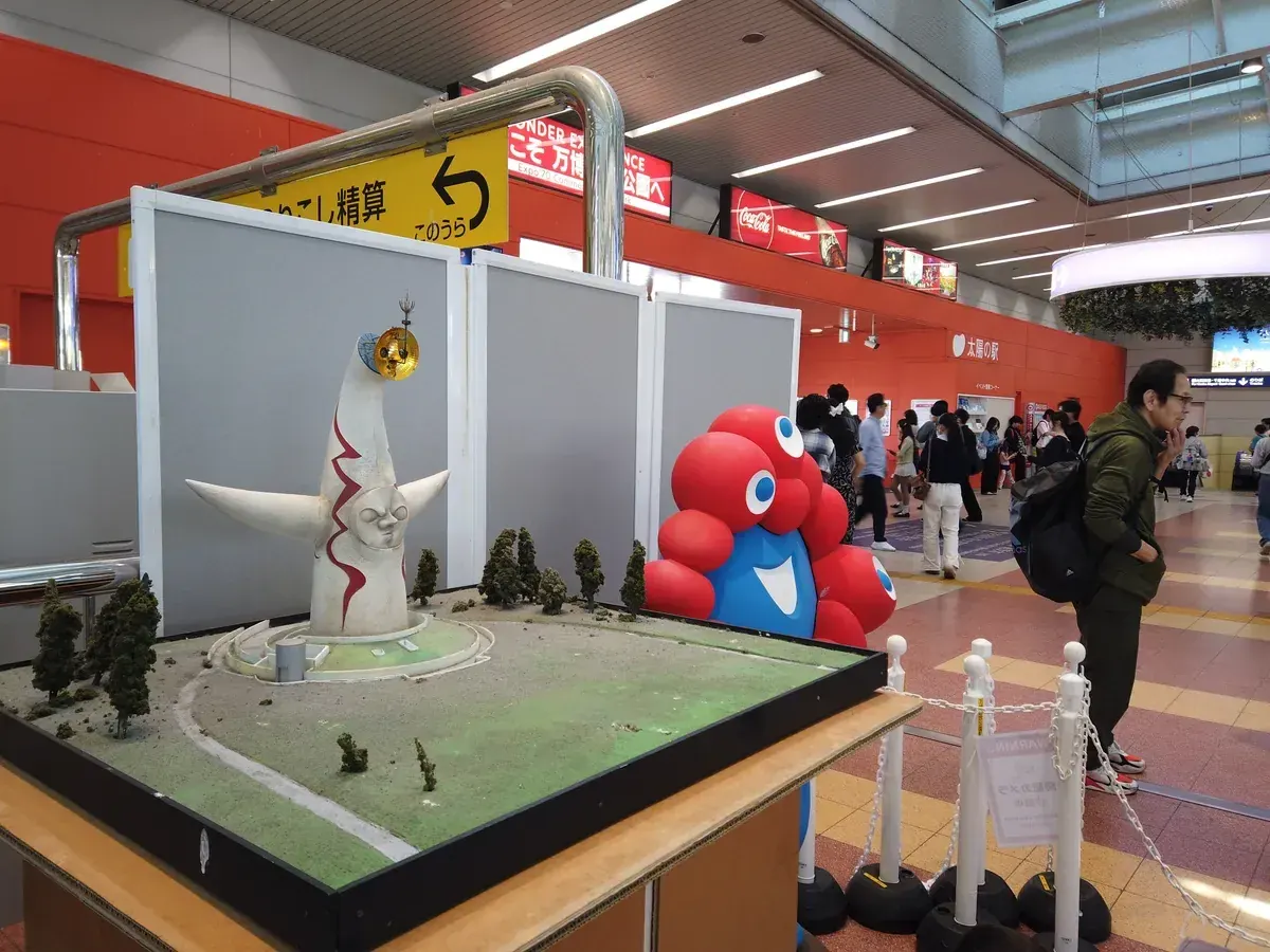 駅構内に並ぶ太陽の塔のミニチュアモデルとミャクミャクのバルーン