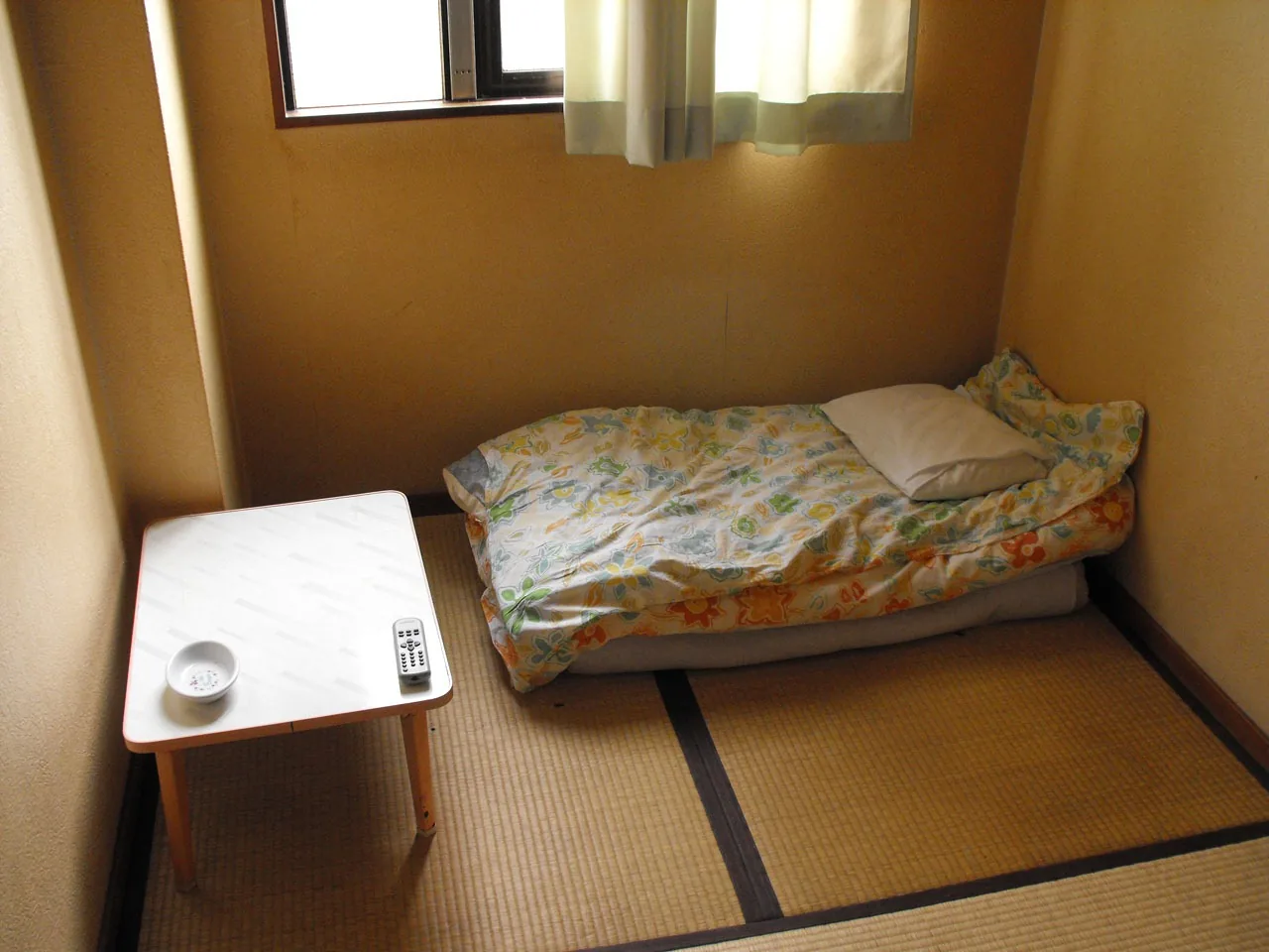 あいりん地区の簡易宿所（ドヤ）の一室。畳と布団、小さなテーブルだけの部屋